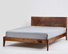 a bed that has been made with wood and white sheets on it, sitting in front of a wall