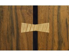 a wooden bow tie on top of a wood cabinet door with black trimmings