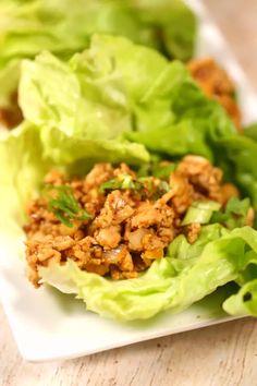 lettuce wraps with meat and seasoning on a white plate sitting on a wooden table