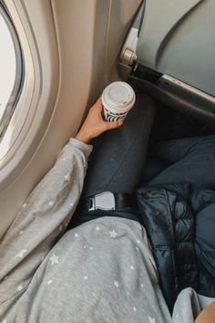 a person laying on an airplane seat with their feet up and holding a coffee cup