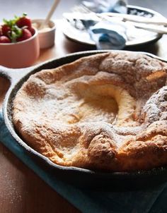 a pie sitting on top of a wooden table next to a bowl of strawberries