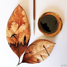 two leaf shaped leaves next to a cup of coffee and a pen on a white surface