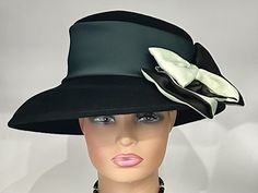 "The featured hat is a  black colored wool winter dress hat.   It has a wide silk band in a forest green color. A gorgeous two tone  bow in black and sage green is placed on an angle. This bow is elegant and classy. The combination of different textures and colors is what makes this hat so charming and disarming. The softness of the bow on the solid black hat is a striking look! This hat can be worn as a winter Church Hat, a Wedding Party Hat, a Tea Party hat,  a Downton Abbey  hat,  winter hat Winter Party Hats With Bow, Formal Black Winter Top Hat, Black Formal Hat For Winter, Fitted Black Wool Cloche Hat, Wide Brim Top Hat For Winter Evening, Black Winter Cloche Hat For Party, Winter Evening Top Hat With Curved Brim, Black Cloche Hat For Winter Party, Black Winter Party Cloche Hat