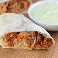 two burritos sitting on top of a wooden cutting board next to a bowl of guacamole