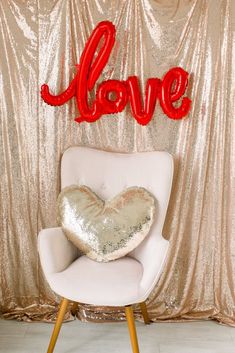 a chair with a heart pillow on it in front of a love sign and gold sequin backdrop