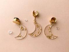 three pairs of gold earrings with crescent and star designs on them, hanging from hooks