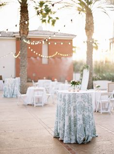 the table is set up for an outdoor wedding reception with lights strung from palm trees