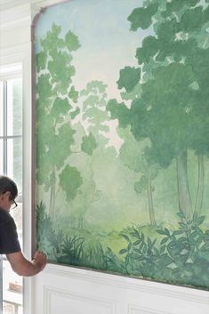 a man painting a mural on the side of a wall in front of a window