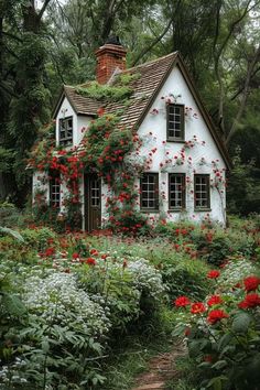 a white house with red flowers growing on it's roof and window frames is surrounded by greenery