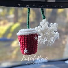 two crocheted mugs hanging from a car dashboard with snowflakes on them