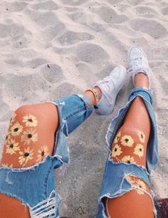 a woman's legs with sunflowers painted on them, sitting in the sand