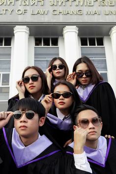 a group of young people standing in front of a building wearing graduation gowns and sunglasses