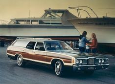 two women standing next to a brown and white station wagon parked in front of a boat