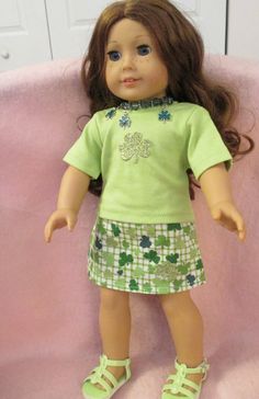 a doll sitting on top of a pink couch next to a green shirt and skirt