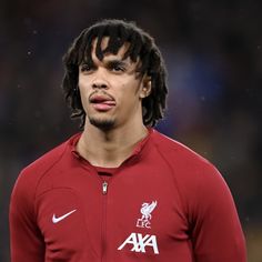 a man with dreadlocks standing in front of a soccer field wearing a red shirt