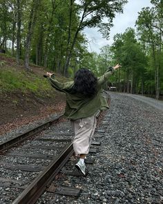 a woman is walking on train tracks in the middle of the woods, with her arms outstretched