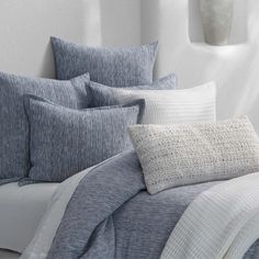 a bed covered in blue and white pillows next to a wall with a vase on it