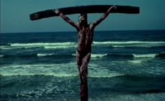 a man standing on top of a wooden cross in front of the ocean with waves