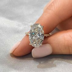 a woman's hand holding an oval shaped diamond ring on top of her finger