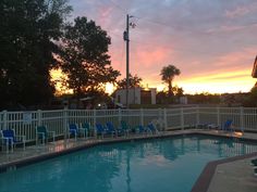 an empty swimming pool at sunset with lounge chairs around the edge and trees in the background