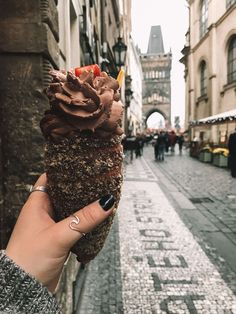 a person holding up an ice cream sundae in the middle of a cobblestone street