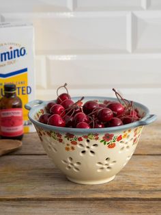 a bowl filled with cherries sitting on top of a wooden table next to a carton of milk