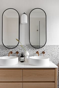 two white sinks sitting next to each other on top of a wooden counter in front of mirrors