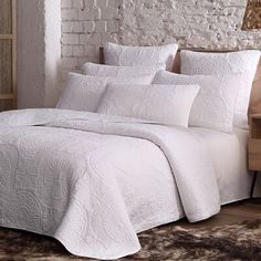 a bed with white sheets and pillows in a room next to a brick wall,