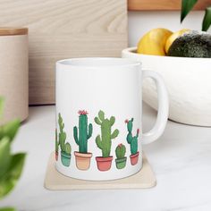 a white coffee mug with cactus designs on it next to some lemons and limes