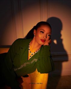 a woman in a green jacket posing for a photo with her shadow on the wall behind her