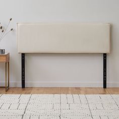 a white headboard sitting on top of a wooden floor next to a table with a potted plant