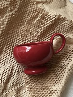 a red cup sitting on top of a table next to a brown cloth covered wall