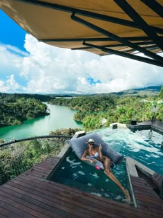 a woman sitting in a hot tub on top of a wooden deck next to a body of water