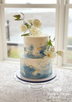 a three tiered cake with flowers on top is sitting in front of a window