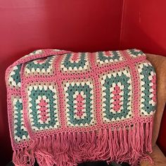 a crocheted blanket sitting on top of a chair next to a red wall