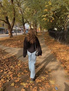 a woman walking down a leaf covered sidewalk