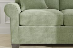 a green couch sitting on top of a hard wood floor next to a white wall