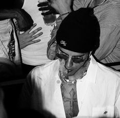 black and white photograph of a man wearing a hat, sunglasses and a tie with other people around him