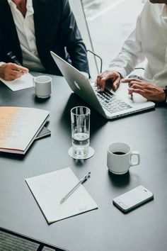 three people sitting at a table with laptops and notebooks in front of them