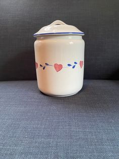 a ceramic jar with hearts on it sitting on a gray surface in front of a black background