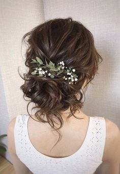 the back of a woman's head with flowers in it and greenery on her hair