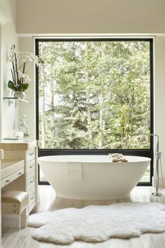 a white bath tub sitting in front of a window next to a desk and chair