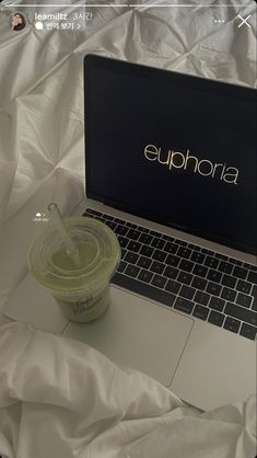 an open laptop computer sitting on top of a white bed next to a plastic cup