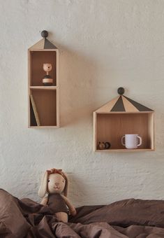 two shelves on the wall above a bed with a teddy bear and coffee cup in it