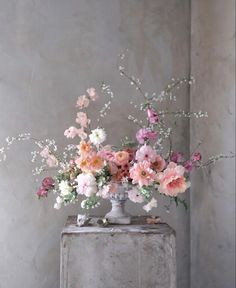 a vase filled with pink and white flowers sitting on top of a wooden table next to a wall