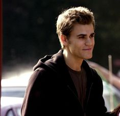 a young man in a black hoodie is looking at the camera while standing next to a white car