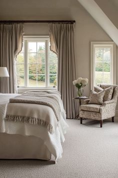 a large bed sitting under two windows in a bedroom next to a chair and lamp