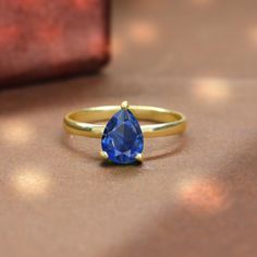 a gold ring with a blue tear shaped stone sitting on top of a wooden table