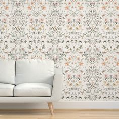 a white couch sitting in front of a wallpapered with flowers and leaves on it