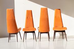 three orange chairs sitting next to each other in front of a white wall and floor